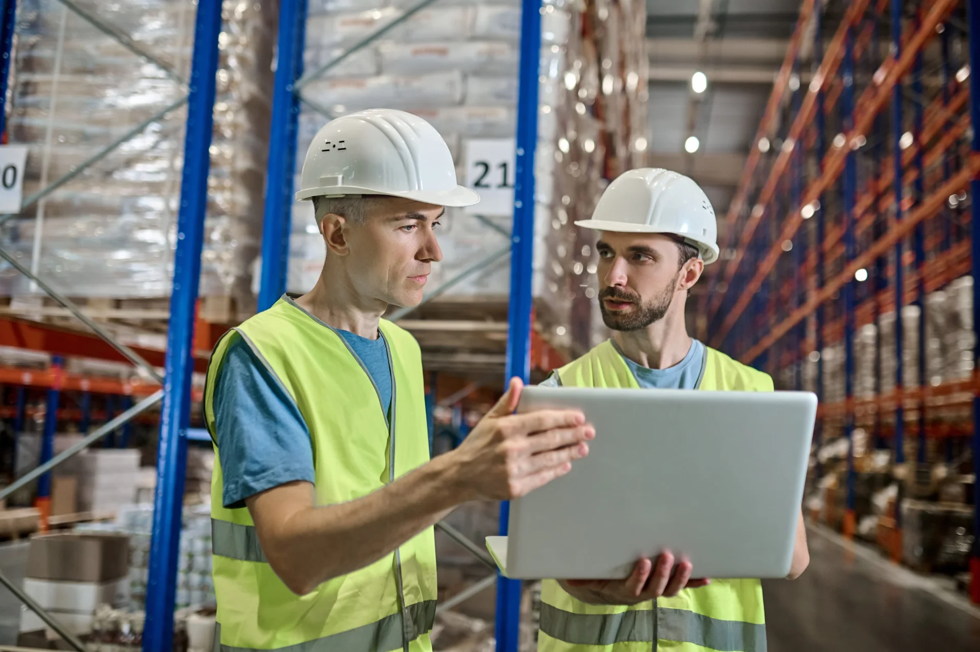 two-men-overalls-with-laptop-talking-warehouse two-men-overalls-with-laptop-talking-warehouse